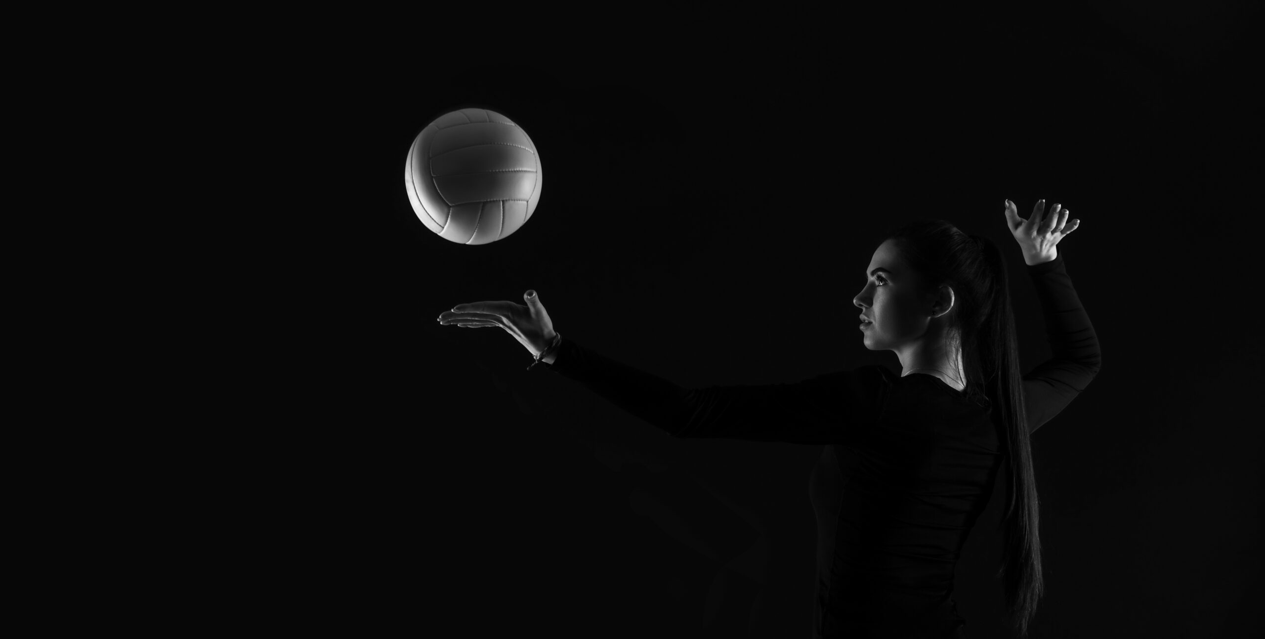 Volleyball girl kick ball on dark background. Player doing sport workout online. Sport and recreation concept. Black and white color filter